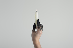 Cropped view of witch hand with jewelry ring and black paint holding candle isolated on grey with copy space