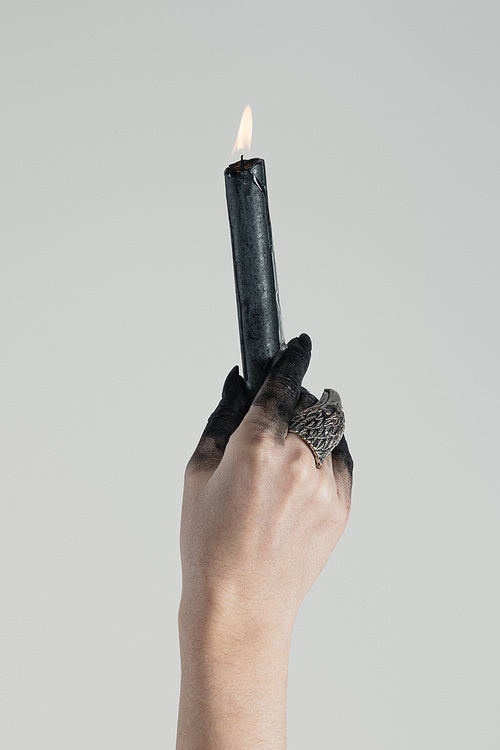Cropped view of black painted hand of witch with jewelry ring holding candle isolated on grey