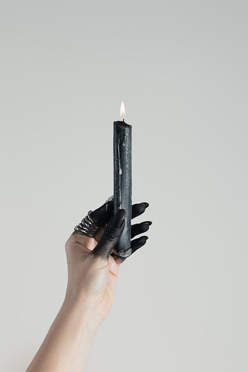 Cropped view of witch holding candle in black painted hand isolated on grey