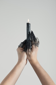 Cropped view of witch with black paint on hands holding burning candle isolated on grey