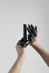 Cropped view of black painted hands of witch with jewelry rings and candle isolated on grey