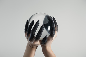 Cropped view of black painted hands of witch holding crystal ball isolated on grey