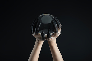 Cropped view of witch hands in black dye holding crystal ball isolated on black