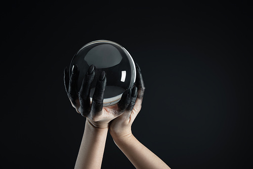 Cropped view of witch with black paint on hands holding crystal ball isolated on black