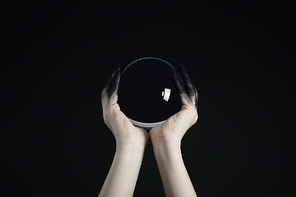 Cropped view of witch holding crystal ball in black painted hands isolated on black