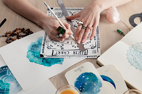Cropped view of astrologer drawing birth chart by watercolor paintings with zodiac signs on cards on table