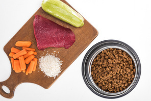 top view of dry pet food and raw meat, , carrot and zucchini on wooden cutting board isolated on white