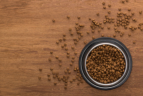 top view of dry pet food in silver bowl and around on wooden table