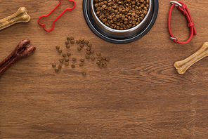 top view of dry pet food in silver bowl near bones, collar and pet toy on wooden table