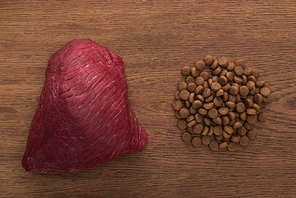 top view of dry pet food near raw meat on wooden table