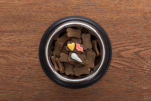 top view of dry pet food in silver bowl with vitamins on wooden table