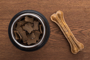 top view of dry pet food in silver bowl near bone on wooden table