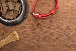 top view of dry pet food in silver bowl near bone, collar on wooden table