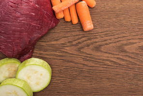 top view of raw meet, zucchini and carrot on wooden table