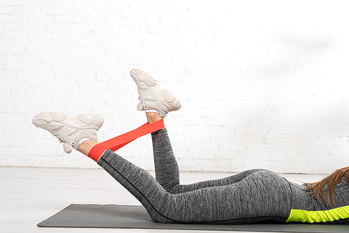 cropped view of sportive woman lying on fitness mat and working out with resistance band