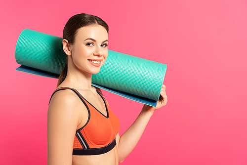 happy sportswoman holding fitness mat isolated on pink