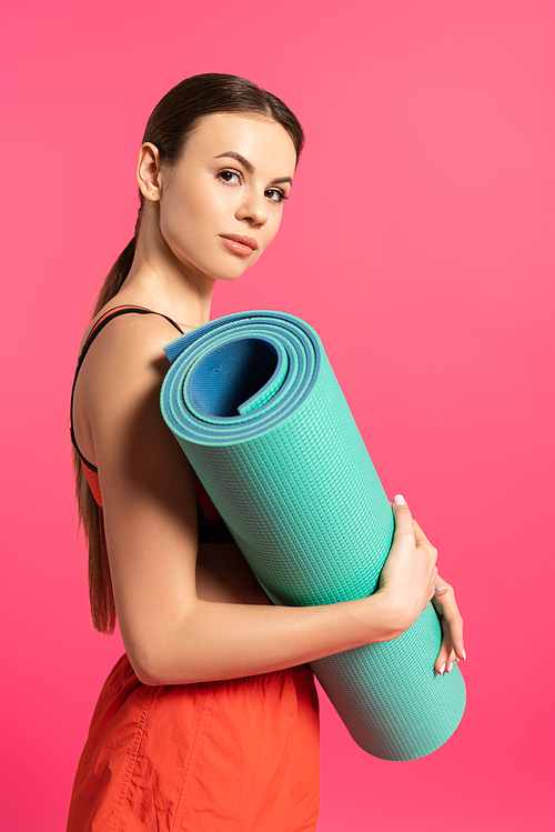 attractive sportswoman holding fitness mat isolated on pink