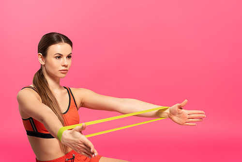 beautiful sportswoman working out with resistance band on pink
