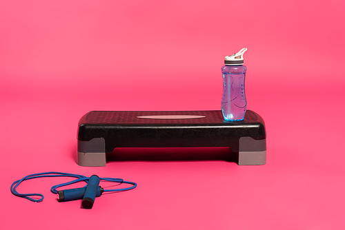 sports bottle with fresh water on step platform near skipping rope on pink