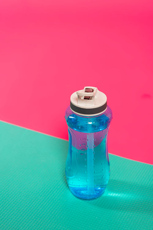 sports bottle with fresh water near fitness mat isolated on pink