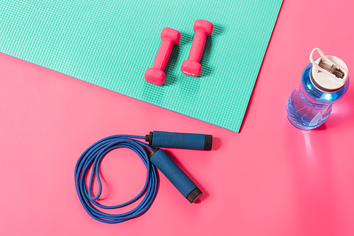 top view of sports bottle with water near skipping rope and dumbbells on fitness mat on pink