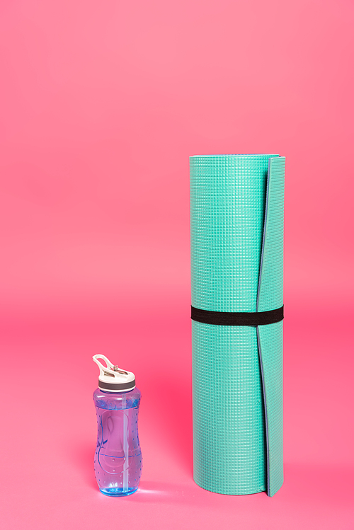 sports bottle with water near fitness mat on pink