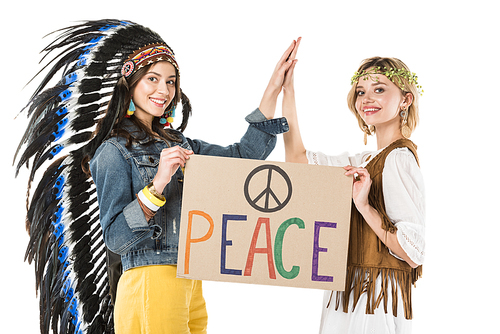 two smiling bisexual hippie girls in indian headdress and wreath holding placard with inscription and touching hands isolated on white