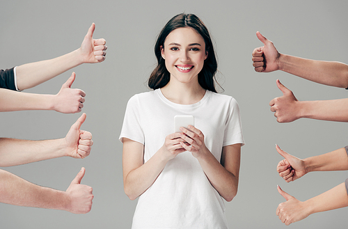 partial view of men and women showing thumbs up near cheerful girl with smartphone isolated on grey