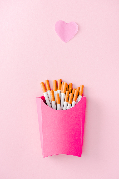 top view of cigarettes packed in paper box on pink with heart symbol, french fries concept