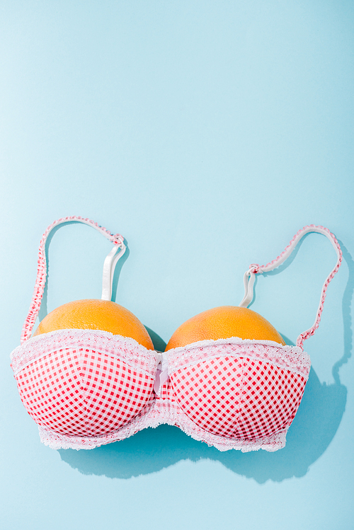 top view of bra with two oranges on blue with copy space, breasts concept