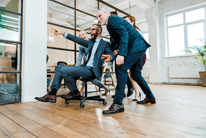 low angle view of cheerful businessman sitting on chair and pointing with finger near multicultural coworkers