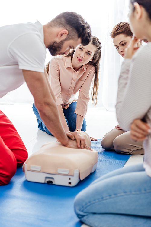 selective focus of instructor performing cpr on dummy during first aid training with group of people