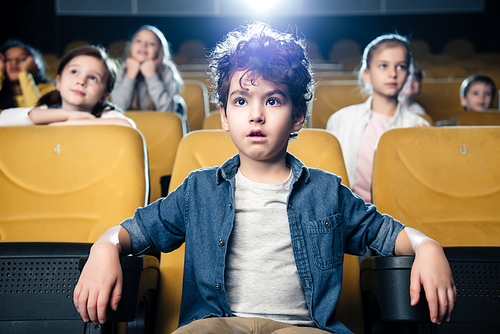 concentrated mixed race boy watching movie in cinema together with multicultural friends