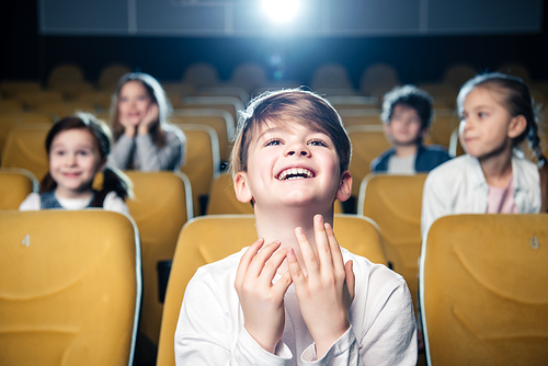 smiling emotional boy watching movie in cinema together with multicultural friends