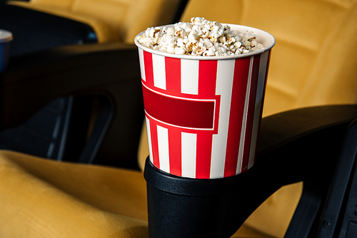 selective focus of cinema seat with stripped paper cup of popcorn in cup holder