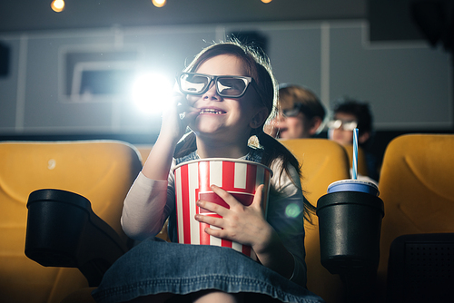 cute smiling child in 3d glasses eating popcorn and watching movie in cinema