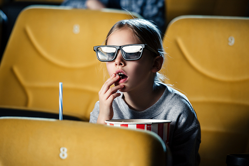 cute attentive child in 3d glasses eating popcorn in cinema
