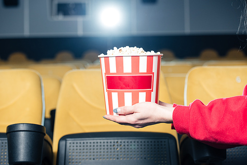 partial view of child holding stripped paper cup with popcorn in cinema