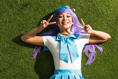 Smiling asian anime girl lying on grass and showing peace signs