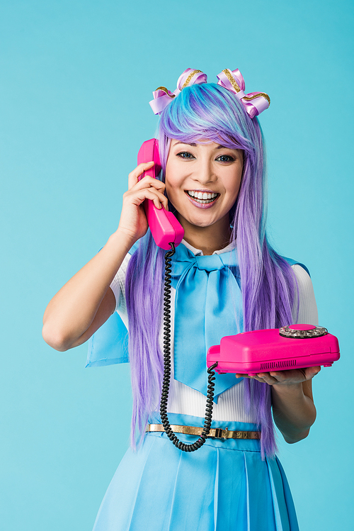 Smiling asian anime girl talking on telephone isolated on blue