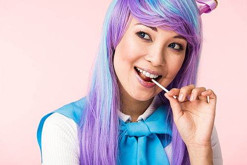 Happy asian otaku girl in wig eating lollipop isolated on pink