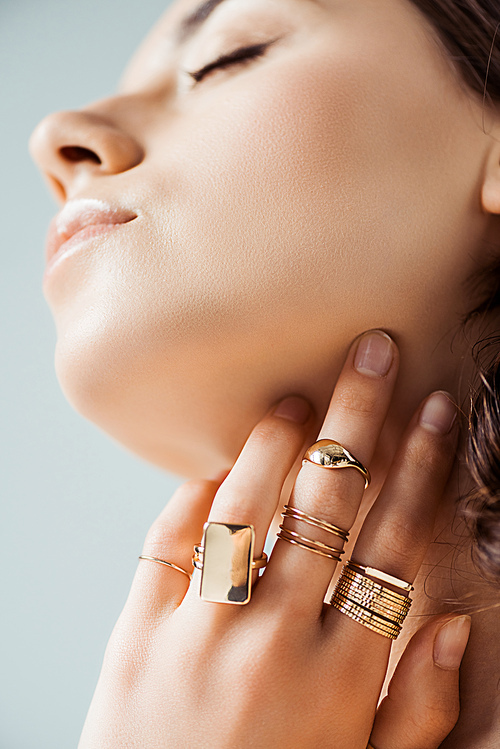 young woman in golden rings touching neck isolated on grey