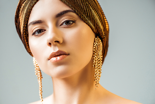 young stylish woman with shiny makeup, golden earrings and turban on head isolated on grey