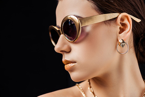 young nude woman in sunglasses, golden earring and necklaces isolated on black