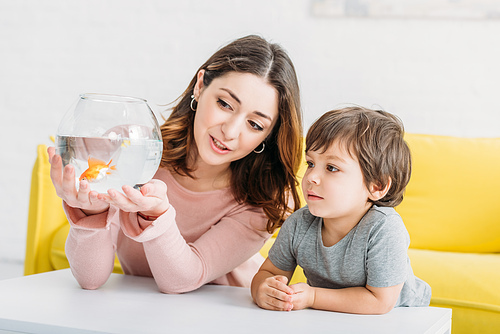 pretty woman holding fish bowl with bright gold fish near adorable son