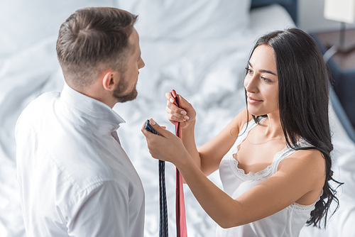 overhead view of cheerful brunette woman holding ties in hands near bearded man