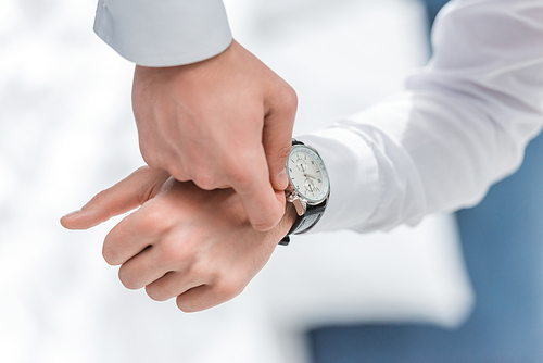 cropped view of man in white shirt touching watch on hand