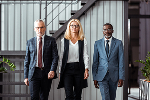 attractive blonde businesswoman walking with handsome multicultural partners in office