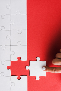 top view of woman pointing with finger at white jigsaw near connected puzzle pieces on red