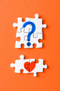 top view of connected puzzle pieces with drawn red heart and blue question mark on orange